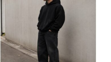 Folded Stussy T Shirt next to Amiri tee and Mixed Emotion rhinestone hoodie on wooden surface